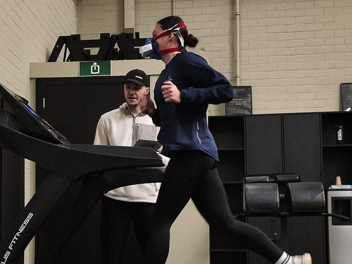 Atleet loopt met ademmasker op de loopband terwijl de coach de looptechniek onder vermoeidheid beoordeelt